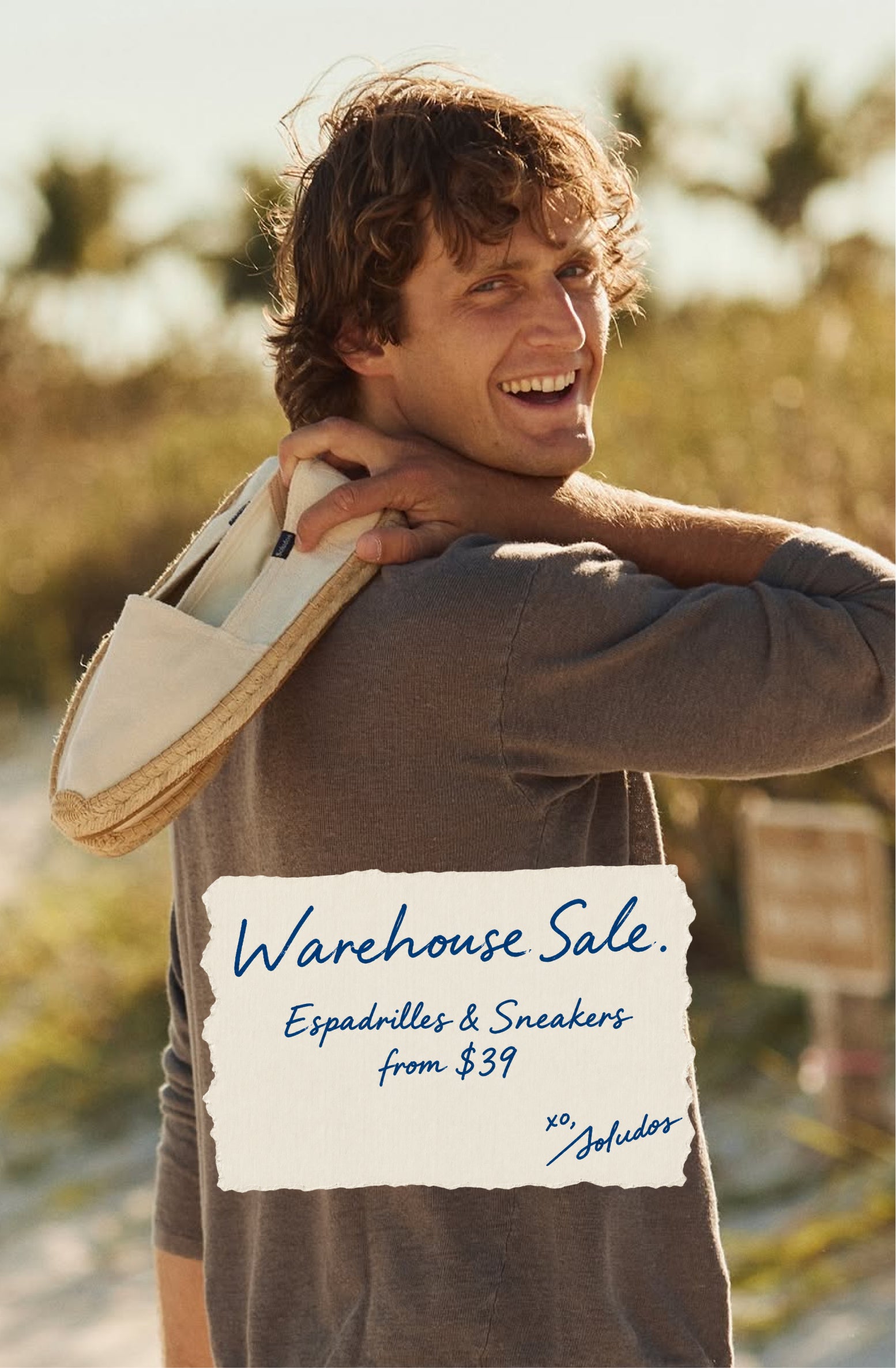 Smiling man holding a beige espadrille outdoors, featuring “Warehouse Sale: Espadrilles & Sneakers from $39” promotional text.
