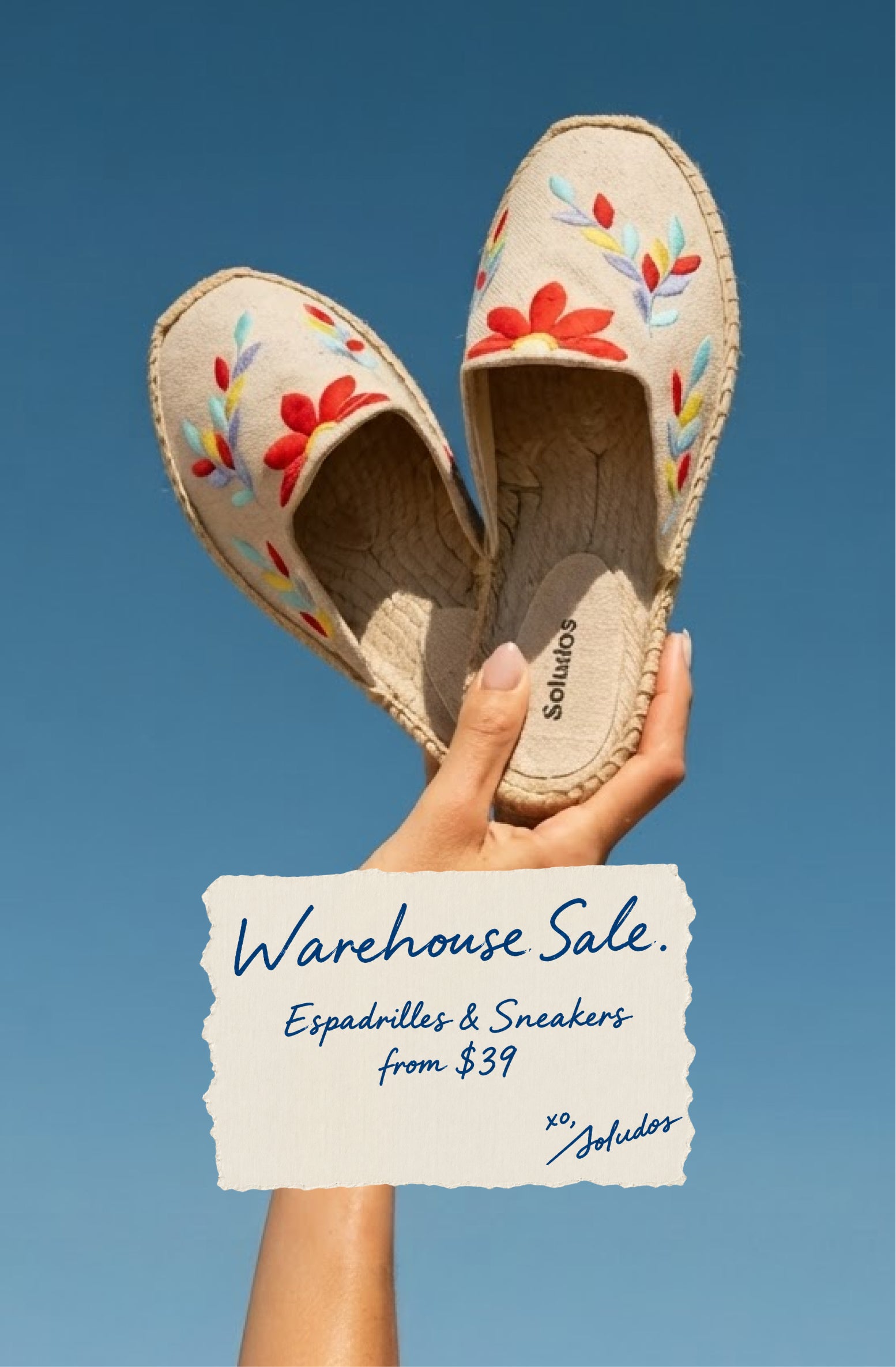 Hand holding beige floral-embroidered espadrilles against a blue sky, featuring “Warehouse Sale: Espadrilles & Sneakers from $39” promotional text.