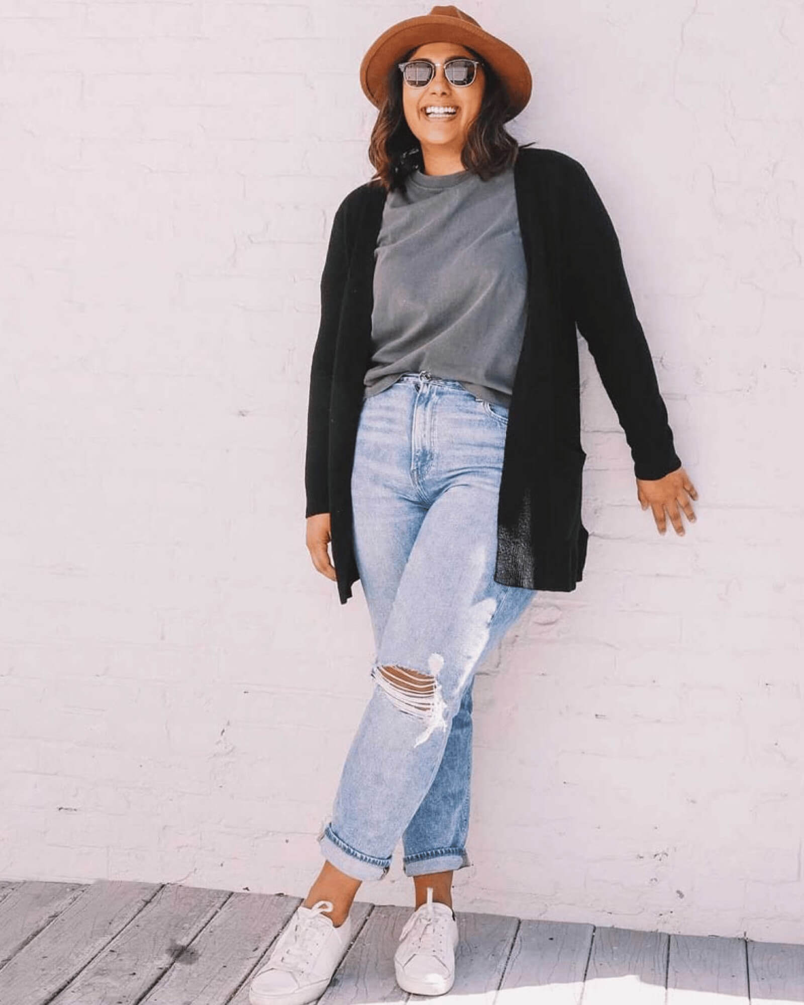 woman leaning on a white wall wearing white Ibiza Sneakers, jeans, and black sweater