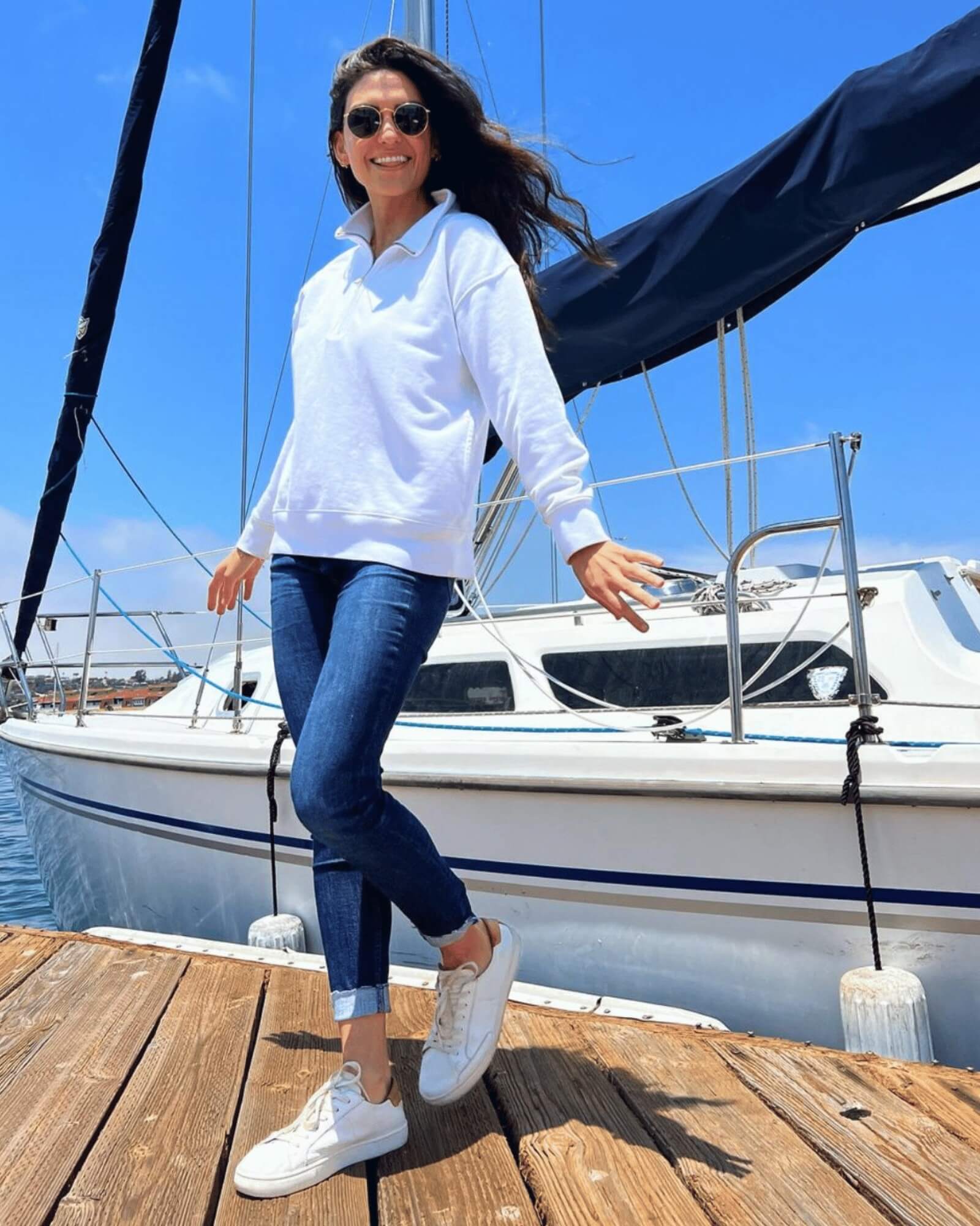woman on boat pier wearing white ibiza sneakers and a quarter zip sweater