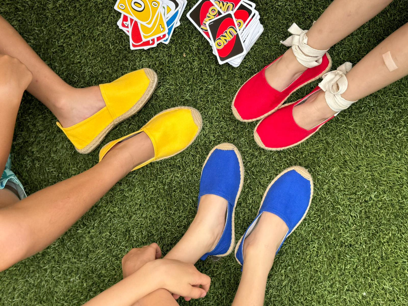 Three kids wearing espadrilles of different colors and playing Uno cards
