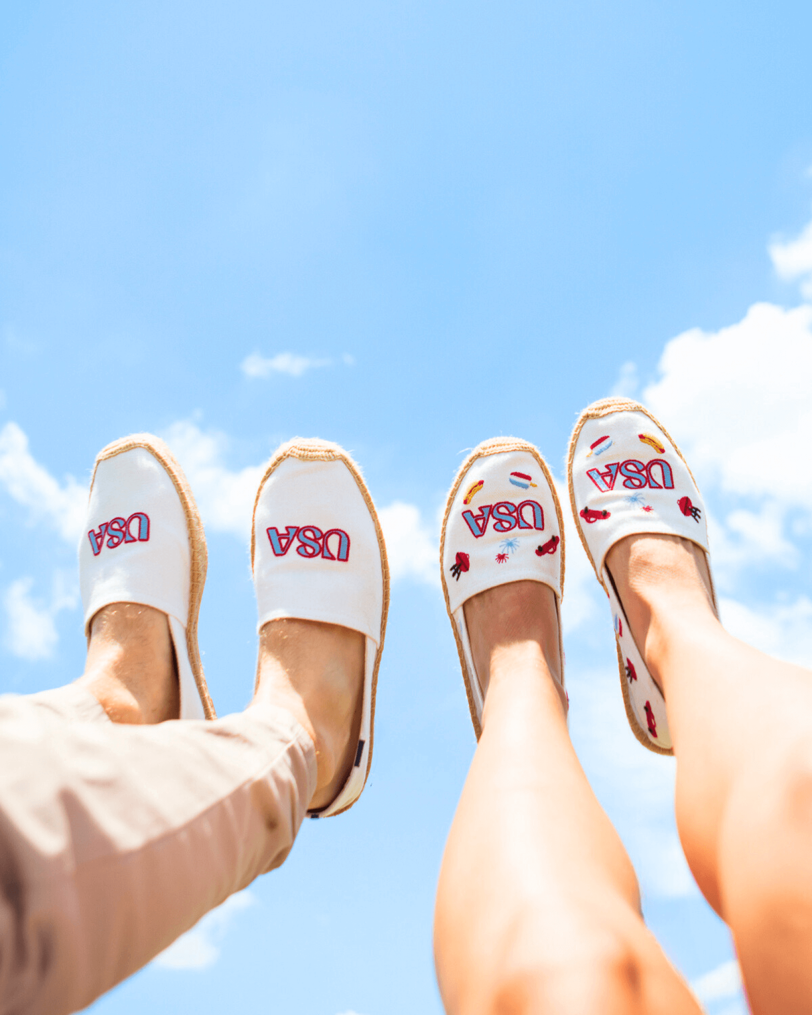 Man and woman wearing white espadrilles embroidered with USA designs with their legs up against the sky
