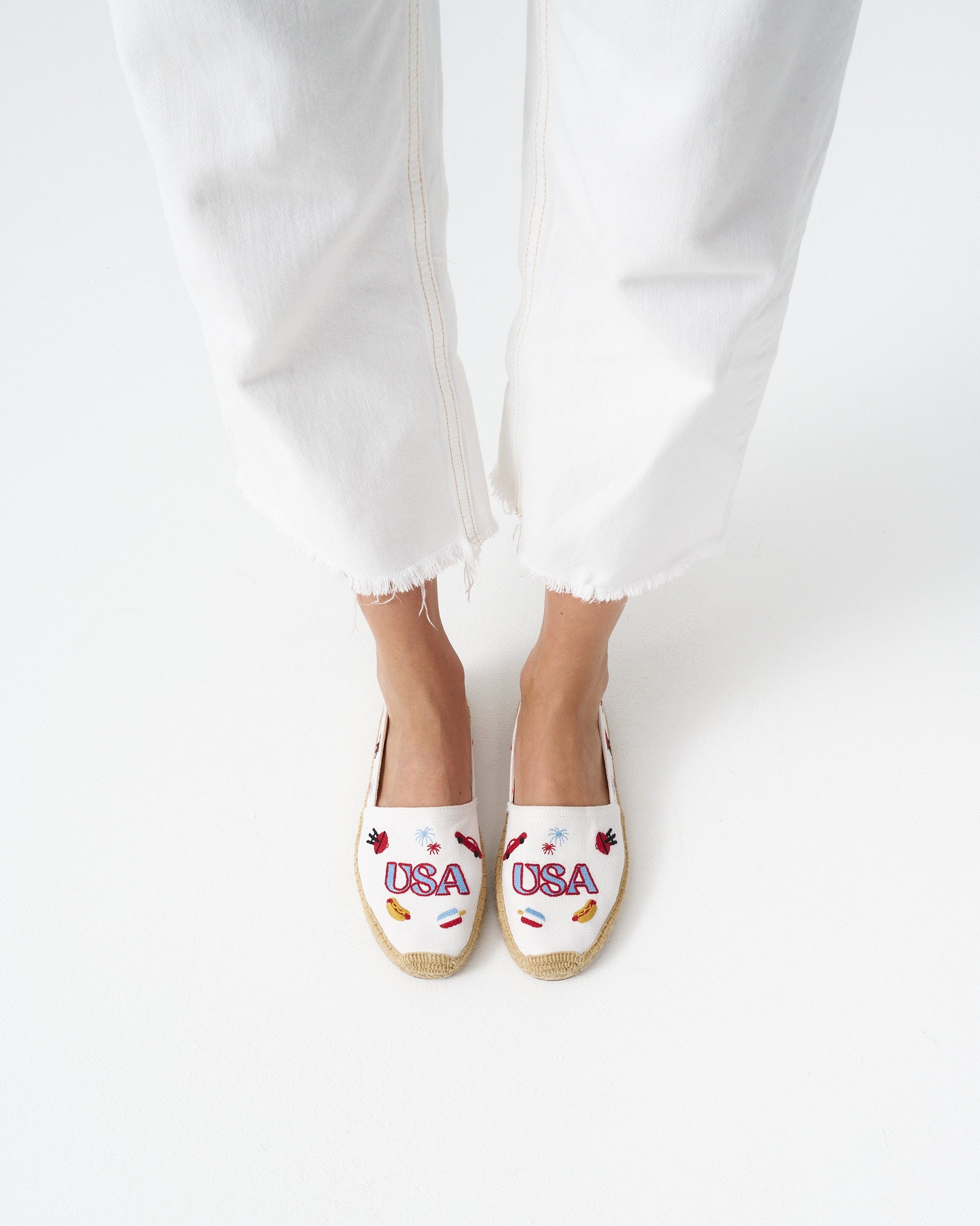 Overhead view of woman wearing white espadrilles with colorful USA embroidery on them